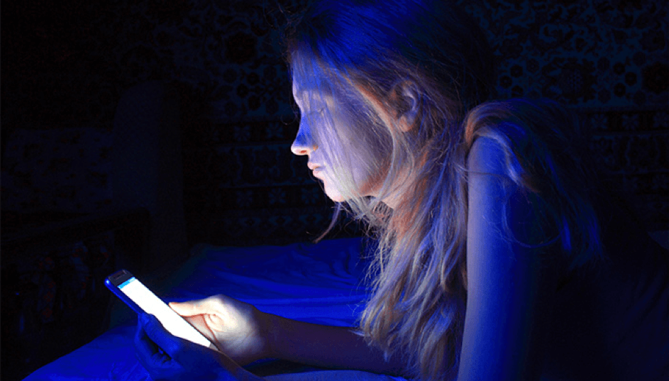 Meisje met telefoon in bed, blauw licht wat kan leiden tot keto slapeloosheid
